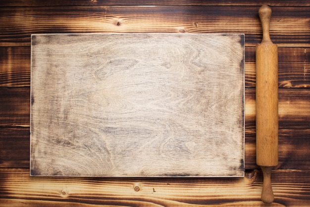 Cutting board and rolling pin at rustic wooden plank background, top view