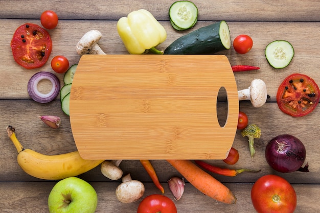 Cutting board surrounded by different fruits and vegetables