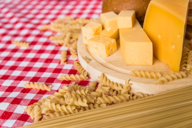 Cutting board with fresh cheese near scattered pasta on table