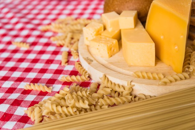 Cutting board with fresh cheese near scattered pasta on table