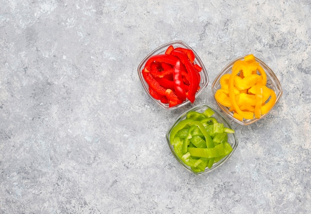 Cutting board with slices of colorful bell peppers on light surface. Sliced sweet peppers in different colors, vegetable salad ingredient, cooking healthy food, top view