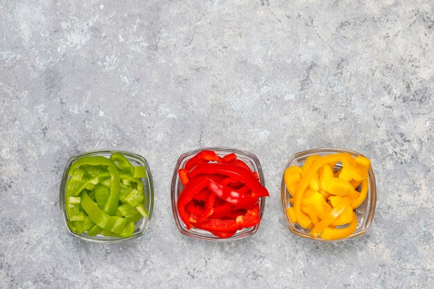 Cutting board with slices of colorful bell peppers on light surface. Sliced sweet peppers in different colors, vegetable salad ingredient, cooking healthy food, top view