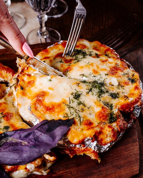 Cutting food with melted cheese and herbs with cutlery.