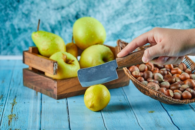 Cutting lemon on blue table with wooden basket of apples and nuts . 