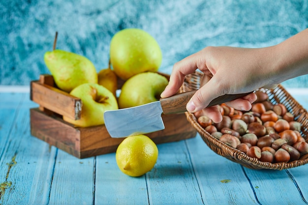 Разрезание лимона на синем столе с деревянной корзиной яблок и орехов.