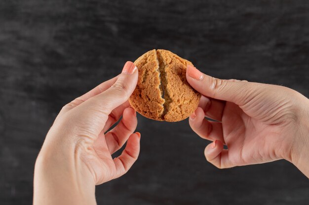 Cutting an oatmeal cookie in the hand into two pieces.