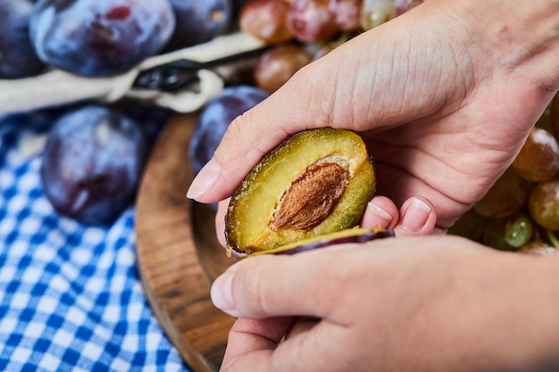 Cutting plum with a bunch of grapes and plums on wooden plate .