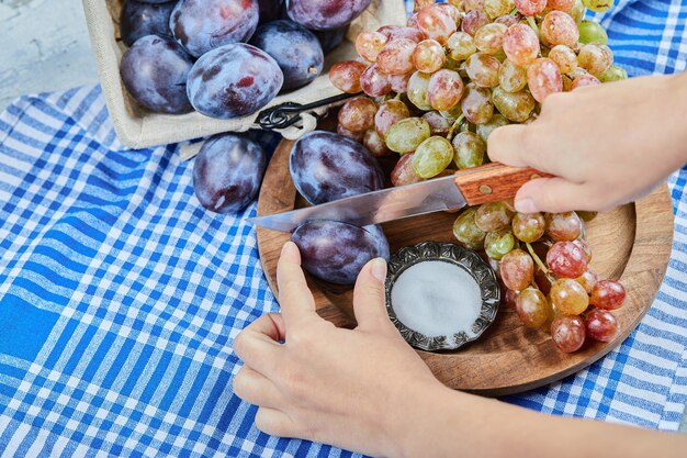 Cutting plum with a bunch of grapes on a wooden plate . High quality photo