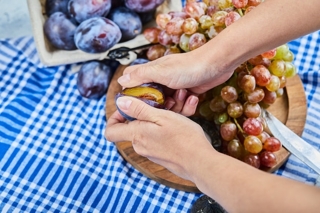 Cutting plum with a bunch of grapes on wooden plate .