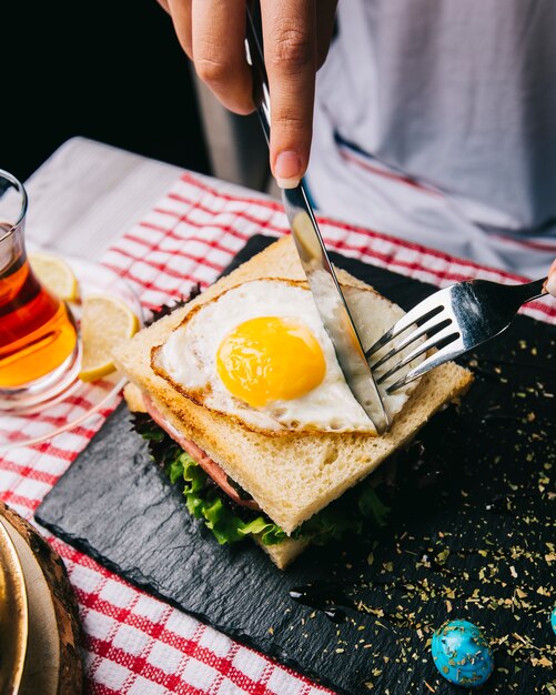 Foto gratuita panino di taglio con uovo fritto con coltello e forchetta.