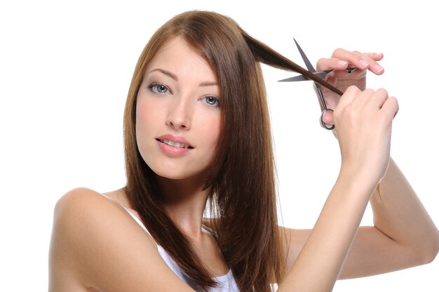 若い美しいブルネットの女性の髪をはさみで切る