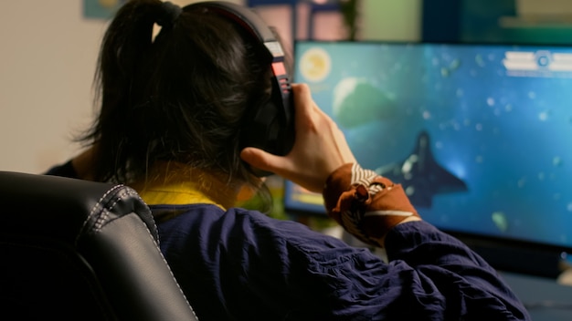 Cyber gamer playing space shooter video game using RGB keyboard and professional headset during gaming tournament. Player talking with multiple players using headphones while streaming video games