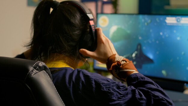 Кибер-геймер играет в космический шутер, используя клавиатуру RGB и профессиональную гарнитуру во время игрового турнира. Игрок разговаривает с несколькими игроками в наушниках во время потоковой передачи видеоигр