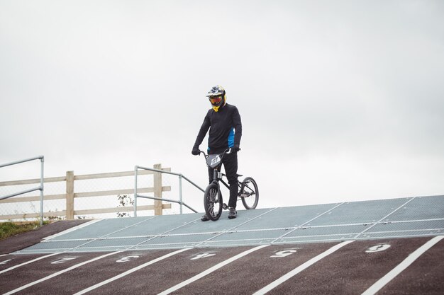 Cyclist standing with BMX bike at starting ramp