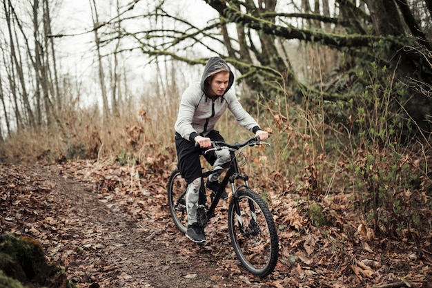 サイクリストは、森林のフード付きトップライド自転車を着て