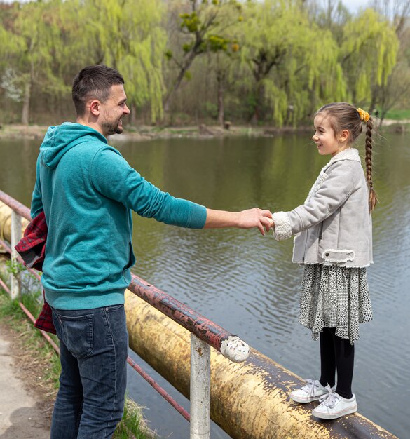 Dad and daughter look into each other's eyes and hold hands while walking in the forest in early spring.