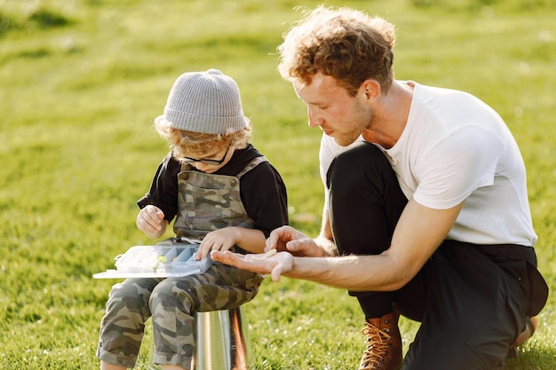 お父さんと彼の男の子は一緒に屋外で時間を過ごします。全体的にカーキ色を着ている巻き毛の幼児の男の子。バケツに座って父親の話を聞いている少年