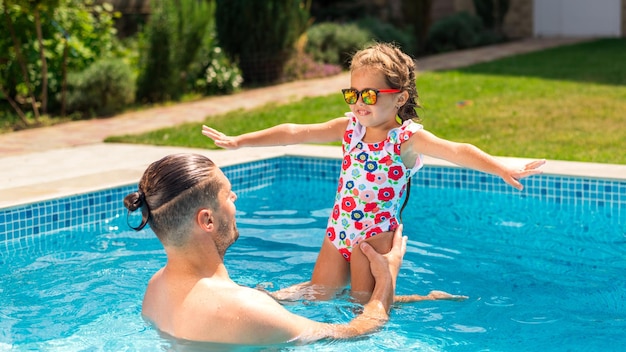 Папа держит свою счастливую дочь на руках в бассейне