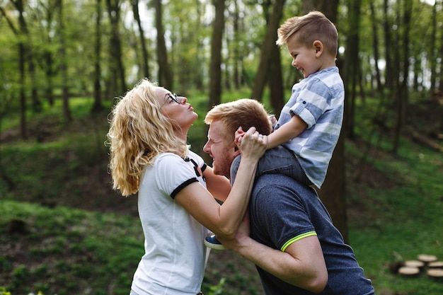 Папа держит сына на шее и играет с мамой в зеленом летнем парке
