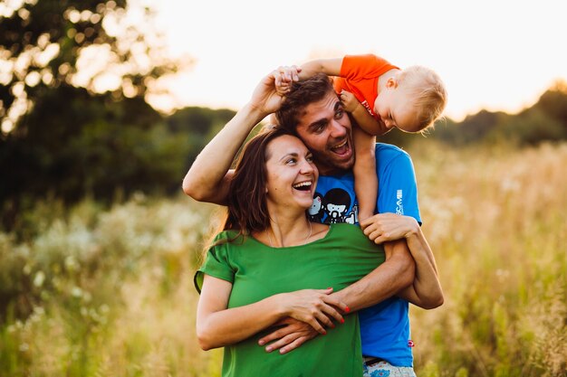 Dad holds little son on the neck hugging young mother from behind