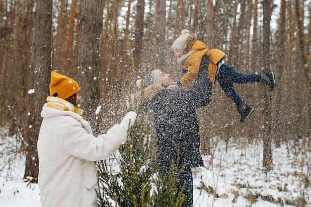 아빠는 겨울 침엽수 숲에서 가족이 산책하는 동안 행복한 어린 아들을 공중으로 들어올립니다. 측면보기