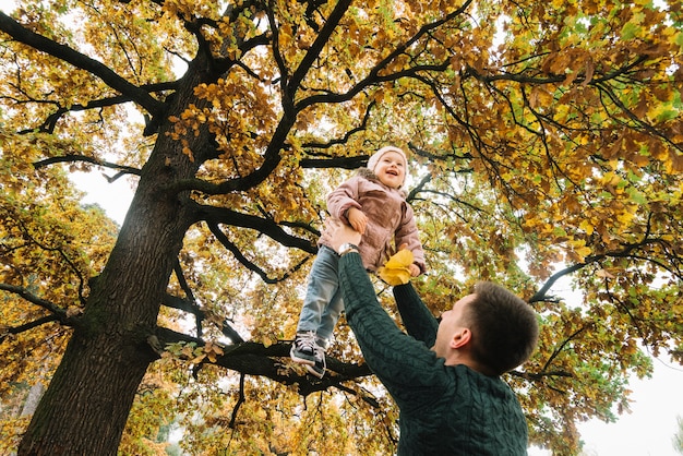 Papà alzando la sua figlia sorridente nella foresta d'autunno