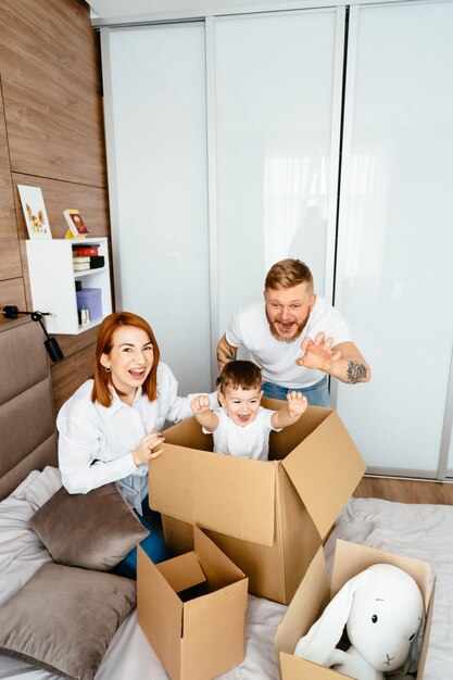 Dad, mom and little son play in the bedroom with paper boxes