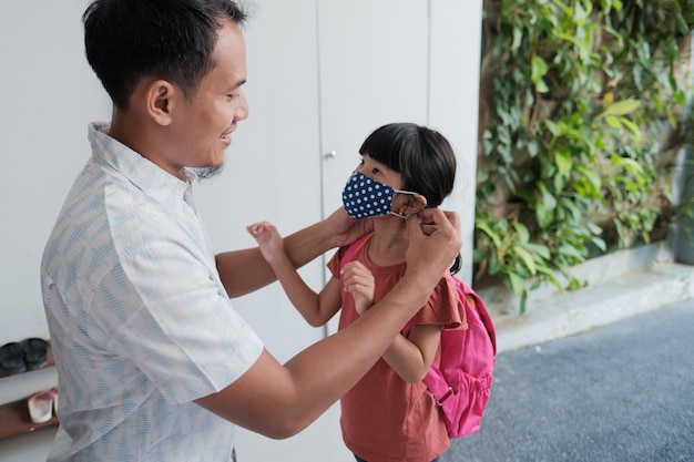 Dad put a mask on her daughter for protection against corona virus before going to the school