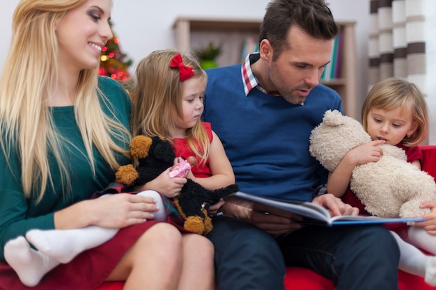 Dad reading book for his little daughters in christmas time