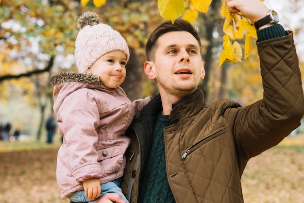 Dad showing autumn leaves his little daughter in park