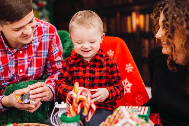 お父さんは、クリスマスと新年の服装の部屋で、柔らかい肘掛け椅子に幸せな小さな息子と座っています