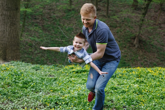 Dad whirls his son like an airplane playing in the green park