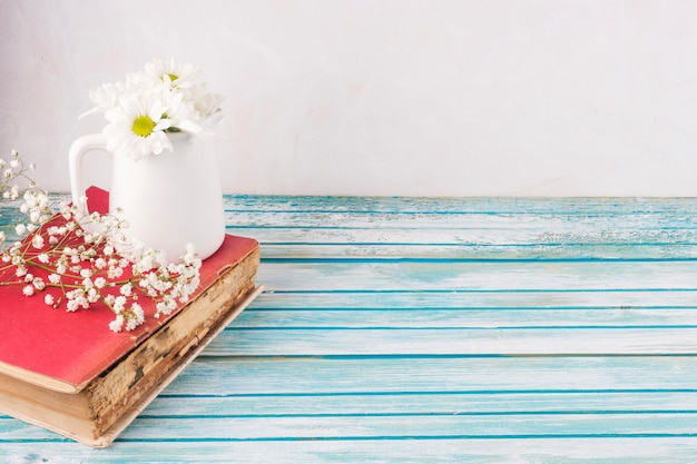 Daisy flowers in white jug on book 