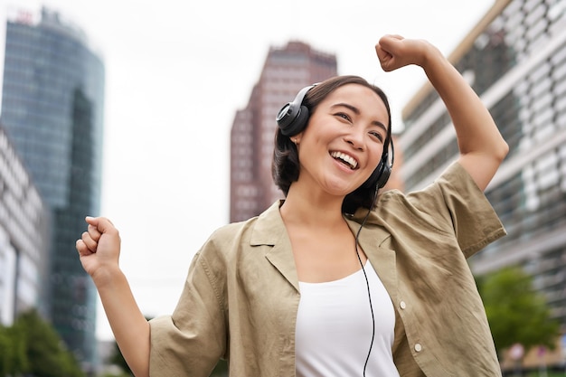 Musica d'ascolto della ragazza asiatica ballante in cuffia che si sente felice in città che si gode all'aperto