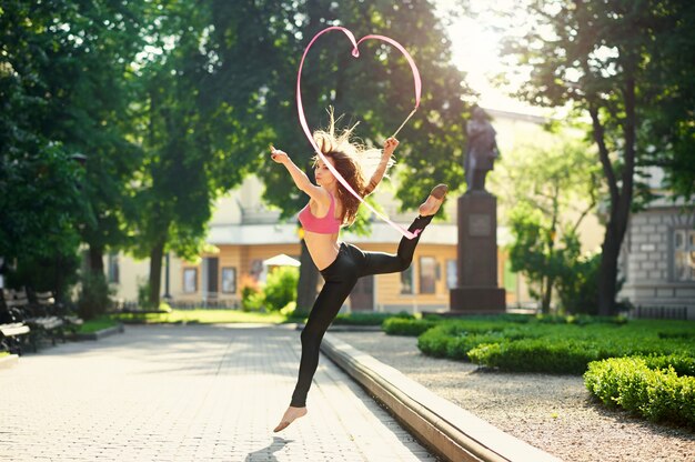 Танцующая девушка делает пируэты с лентой в городском парке.