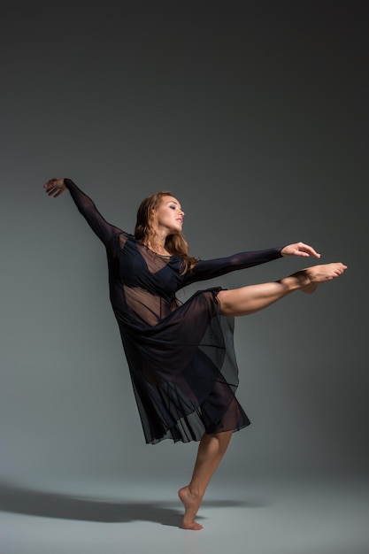 Dancing woman in a black dress. Contemporary modern dance on a gray background. Fitness, stretching model