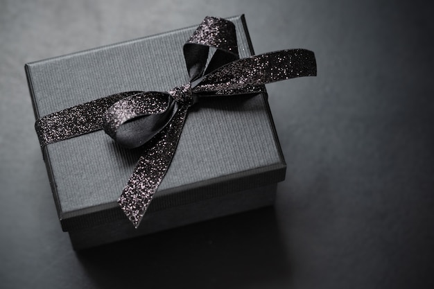 Dark black giftbox with black ribbon on dark background. Closeup