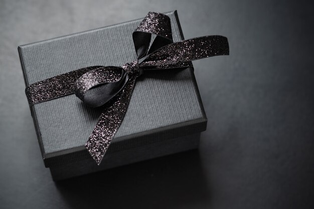 Dark black giftbox with black ribbon on dark background. Closeup