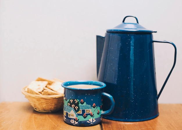 Porcellana blu scuro e tazza da caffè con i cracker sulla scrivania contro il muro