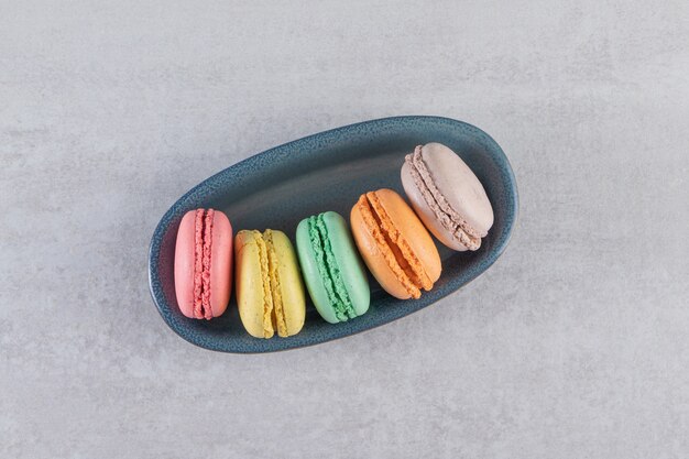 Dark bowl of colorful sweet macaroons on stone table. 