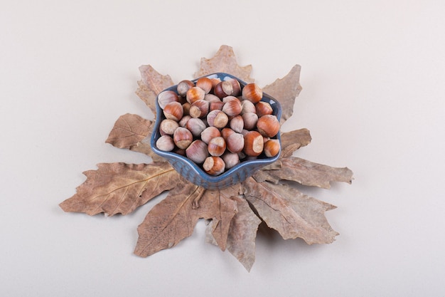 殻から取り出された天然ヘーゼルナッツと白い背景の上の乾燥した葉の暗いボウル。高品質の写真