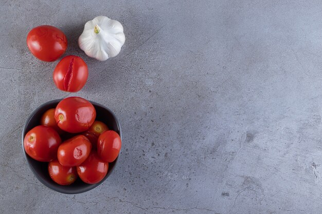절인 토마토의 어두운 그릇은 돌 테이블에 배치됩니다.