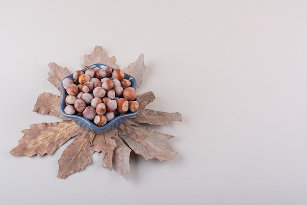 Dark bowl of shelled natural hazelnuts and dry leaves on white background. High quality photo