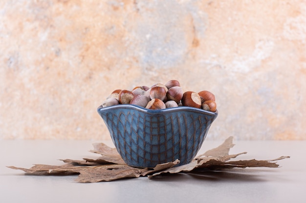 Free photo dark bowl of shelled natural hazelnuts and dry leaves on white background. high quality photo