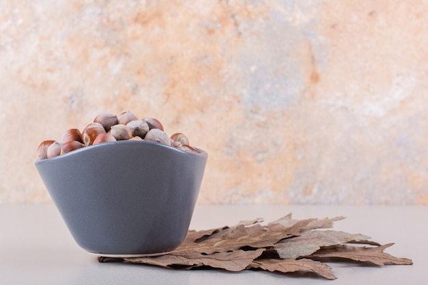 Dark bowl of shelled organic hazelnuts and dry leaves on white background. High quality photo