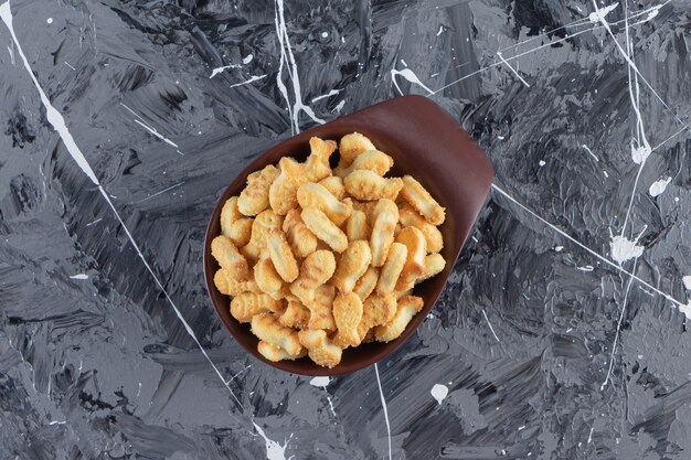 Dark bowl of tasty salted crackers on marble table. 