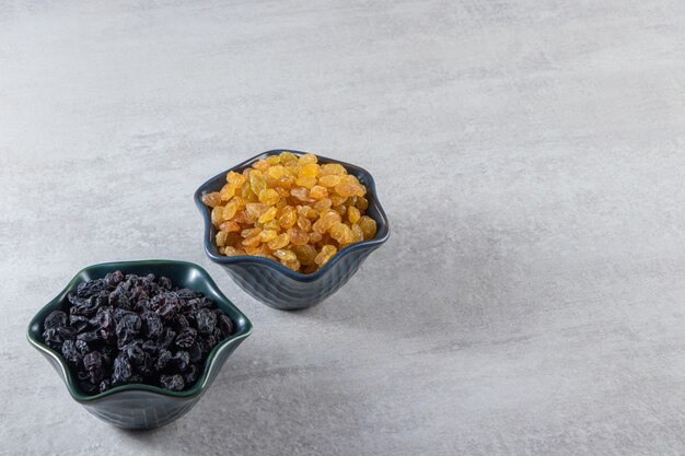 Dark bowls with dried golden and black raisins on stone background. 