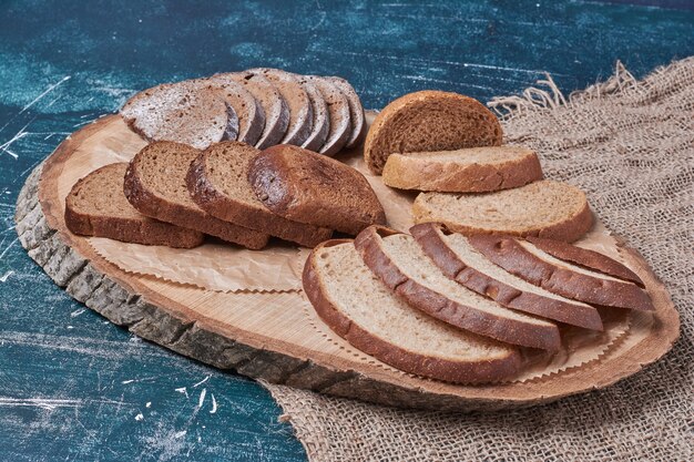 Dark bread slices on wooden board on blue table.