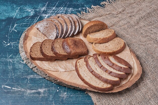 Dark bread slices on wooden board on blue table.
