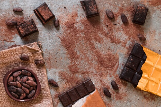 Dark chocolate bar with scattered cocoa powder and beans bowl